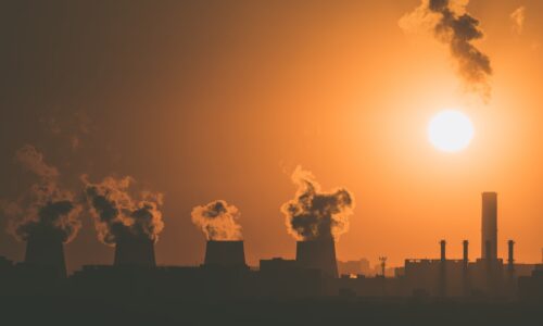 A fossil fuel burning industrial plant silhouetted against the setting sun